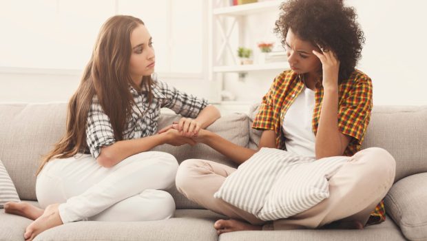 Two women sitting on a couch, one consoling the other