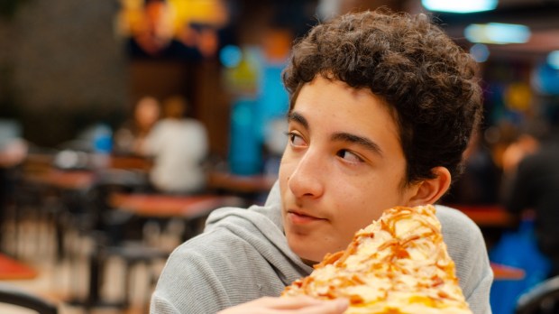 nastolatek je pizzę ze znajomymi w pizzerii i słucha ich rozmowy
