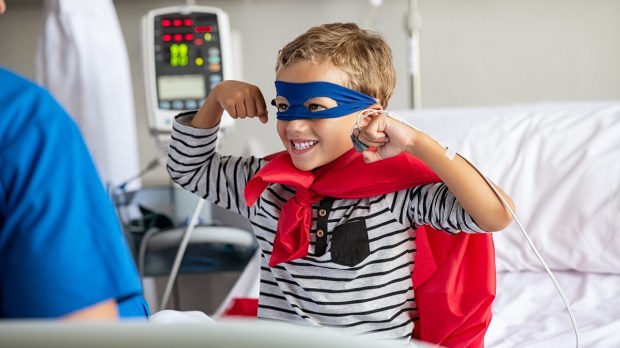 Child dressed as superhero in hospital bed